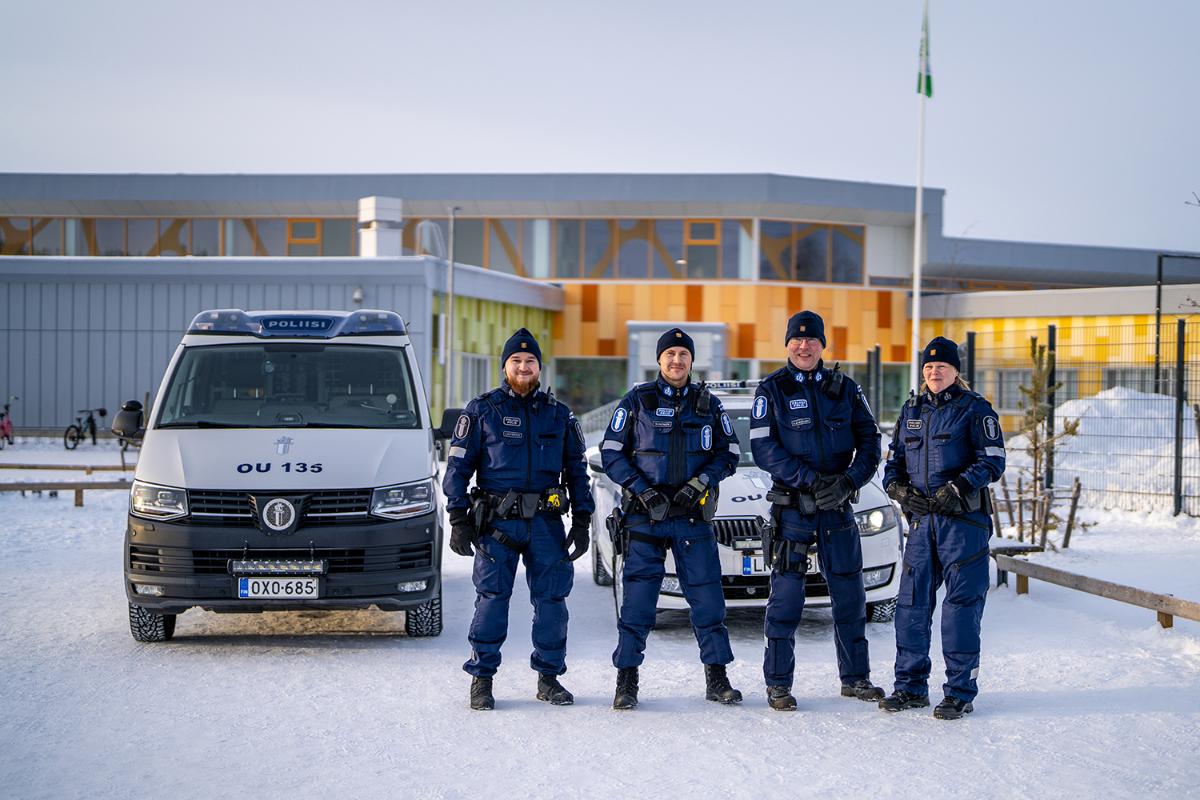 Neljä poliisia seisoo koulurakennuksen edessä talvisessa säässä.