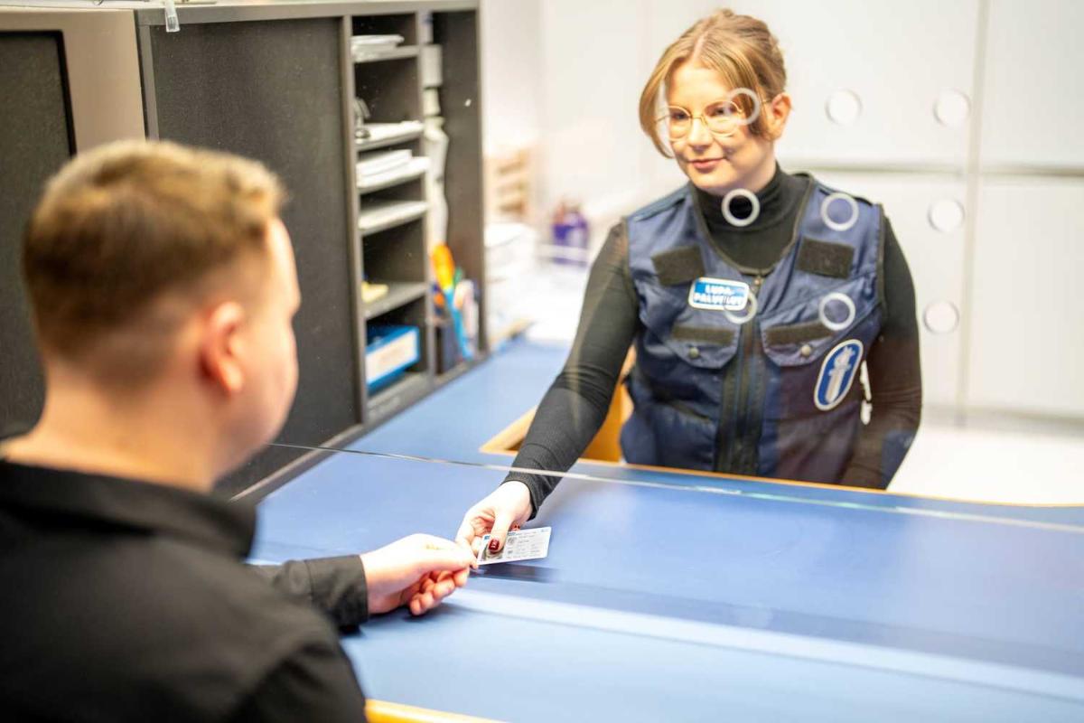 En kvinna räcker ett ID-kort till en kund under glasdörren.