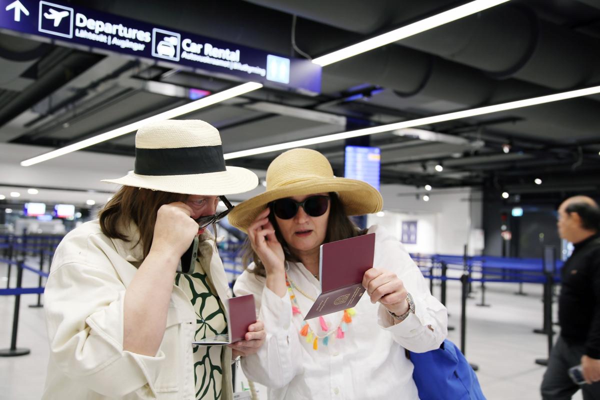 Kaksi naista seisoo lentokentällä ja katsoo passejaan.