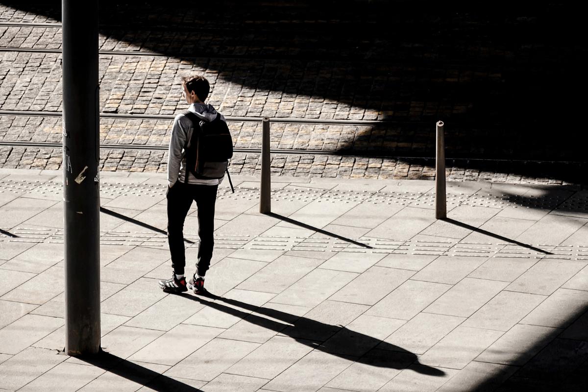 Nuori poika reppuselässä selkä kameraa päin seisoo sillan alla auringossa