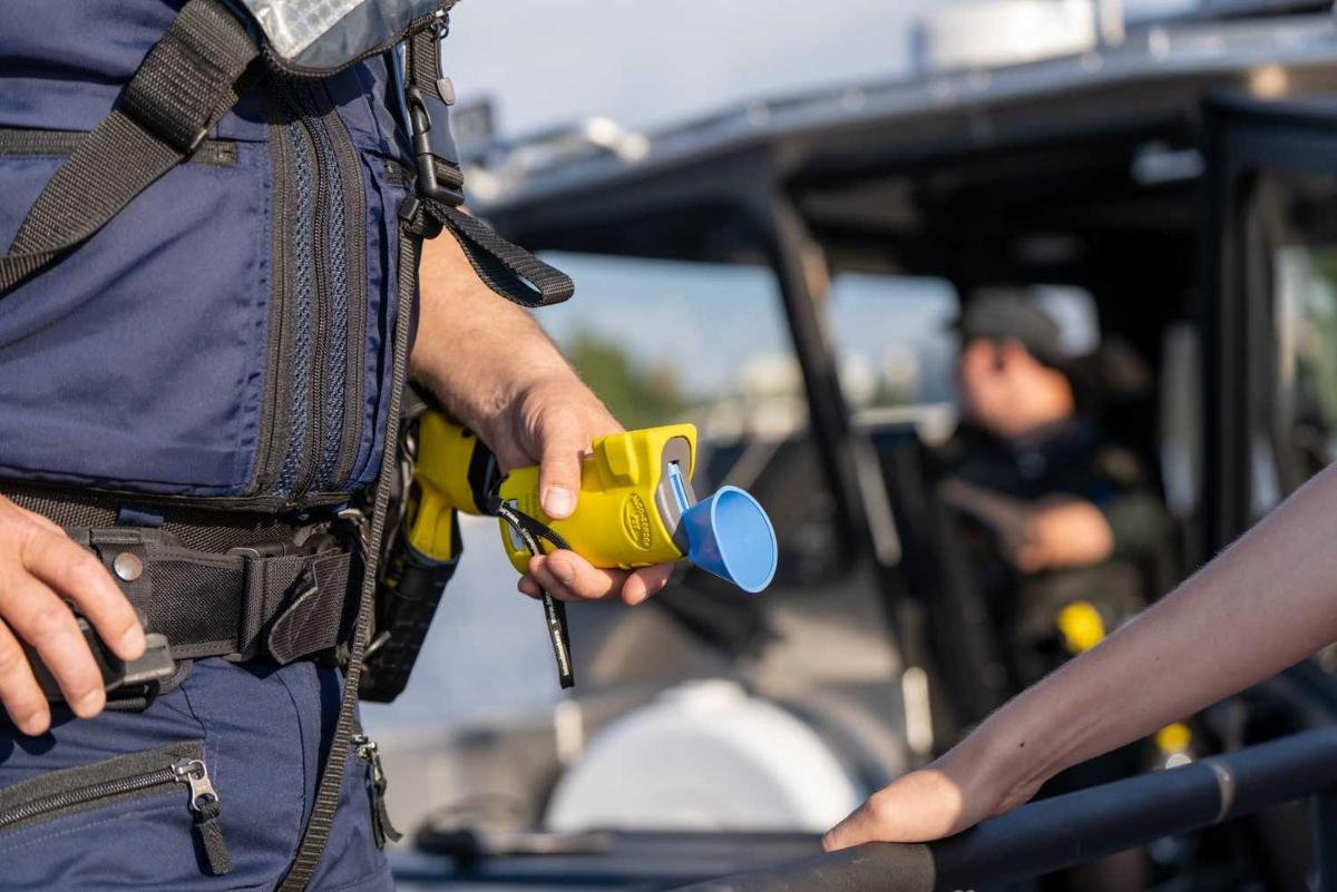 Poliisi päihdevalvontalaite kädessä. Taustalla vene.