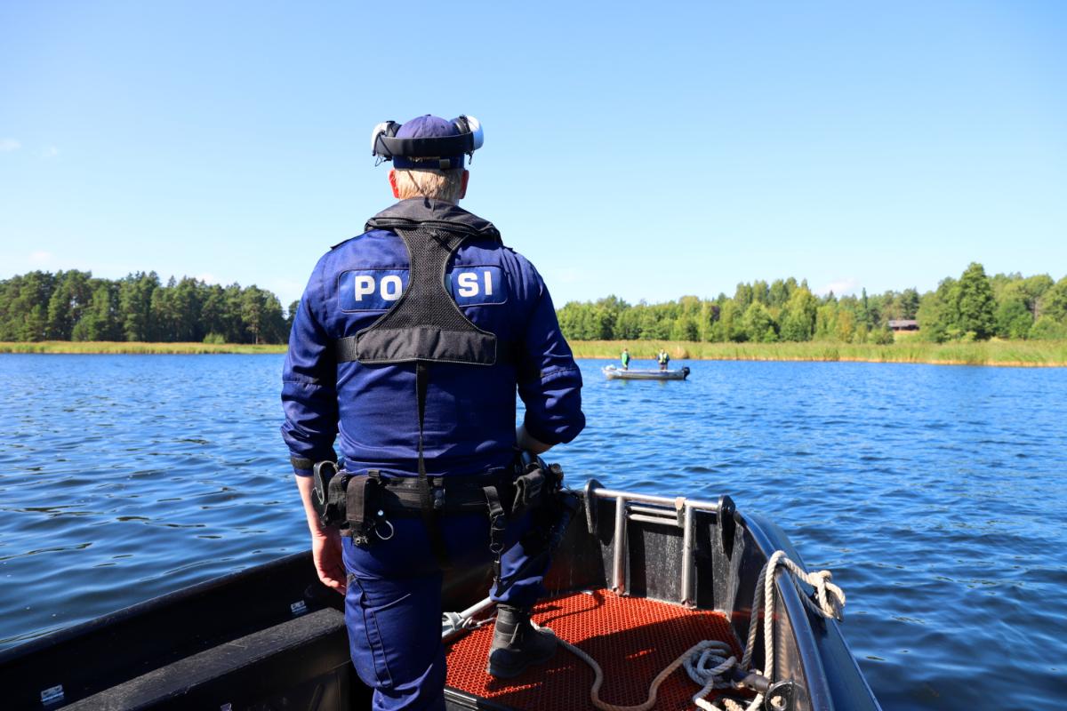 Poliisi seisoo selin veneen etuosassa katsoen merelle.