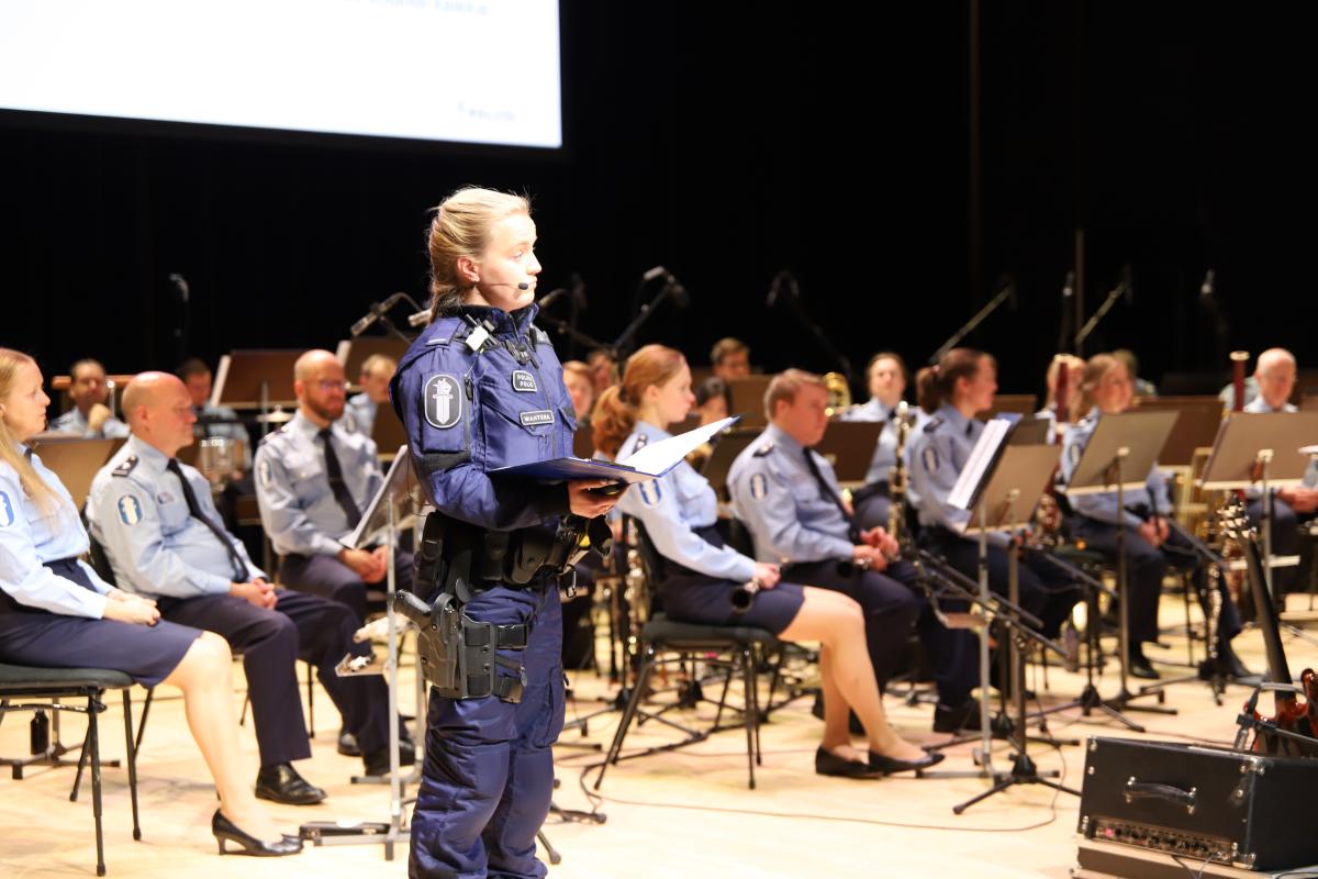Poliisi puhuu orkesterin edessä lavalla virkapuvussa.