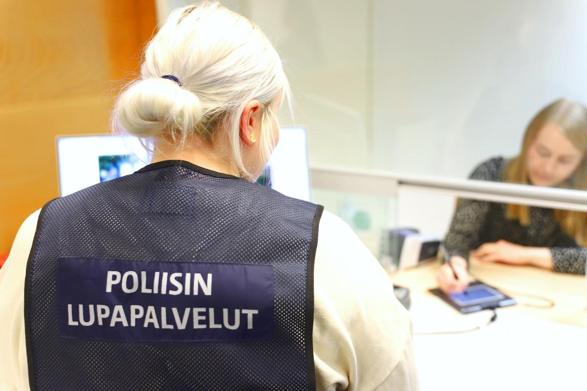 Poliisin lupapalveluiden asiakaspalvelija on selin ja asiakas allekirjoittaa.
