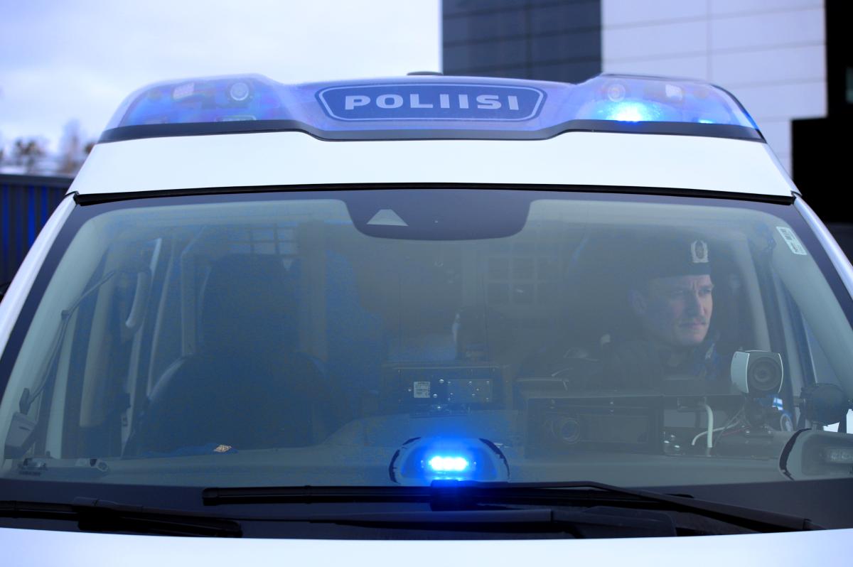 Poliisi näkyy poliisiauton etuikkunan läpi ja auton siniset hälytysvalot välähtävät.