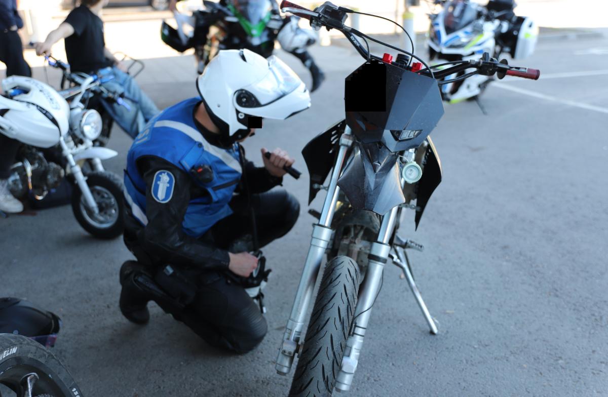 Moottoripyöräpoliisi tarkastelee mopon kuntoa ja taustalla lisää mopoja.