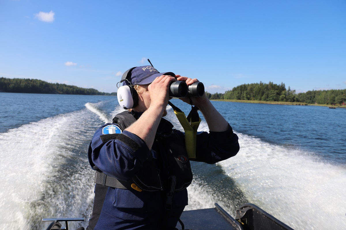 En polisman sitter i båten och tittar med kikare.