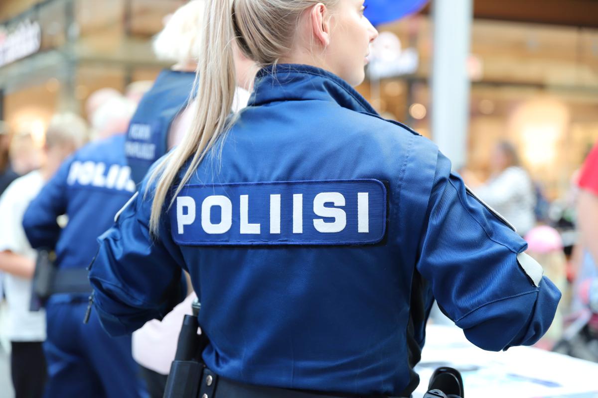 Vaaleahiuksinen poliisinainen seisoo kauppakeskuksessa sininen poliisihaalari yllään.