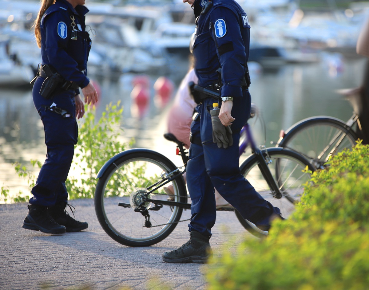 Kaksi poliisia kävelee rannan tuntumassa, ja taustalla joku ajaa polkupyörällä.