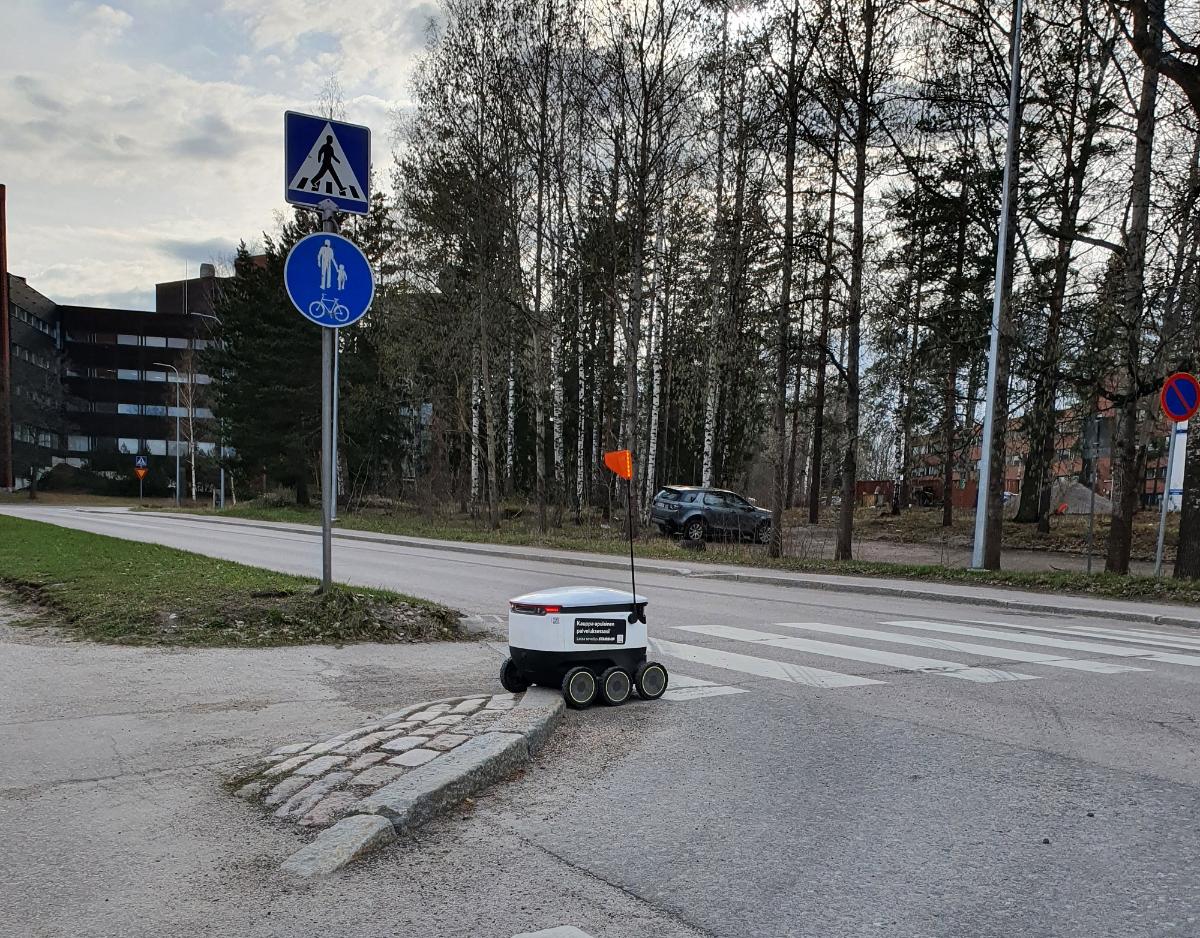 En vit matservicerobot framför ett övergångsställe.