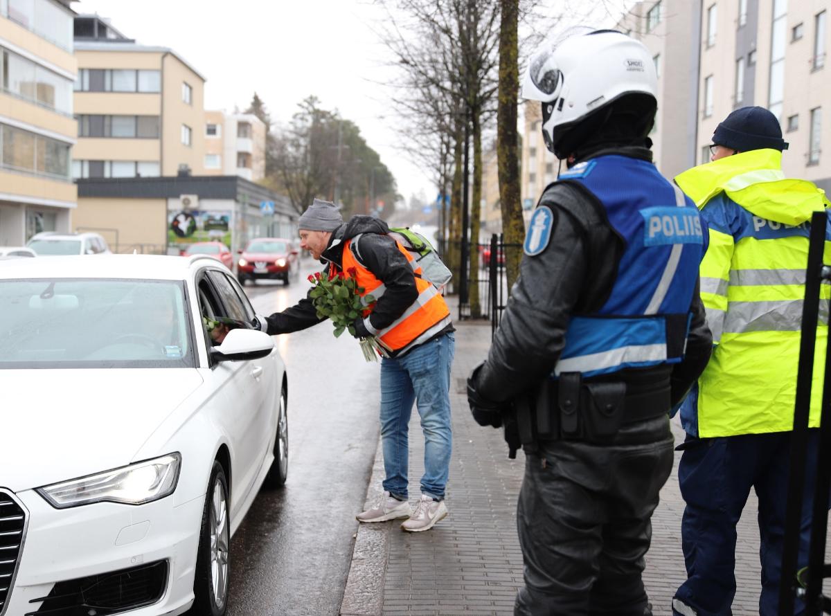 En man räcker en ros till föraren av en bil genom ett bilfönster medan en polis står i bakgrunden.