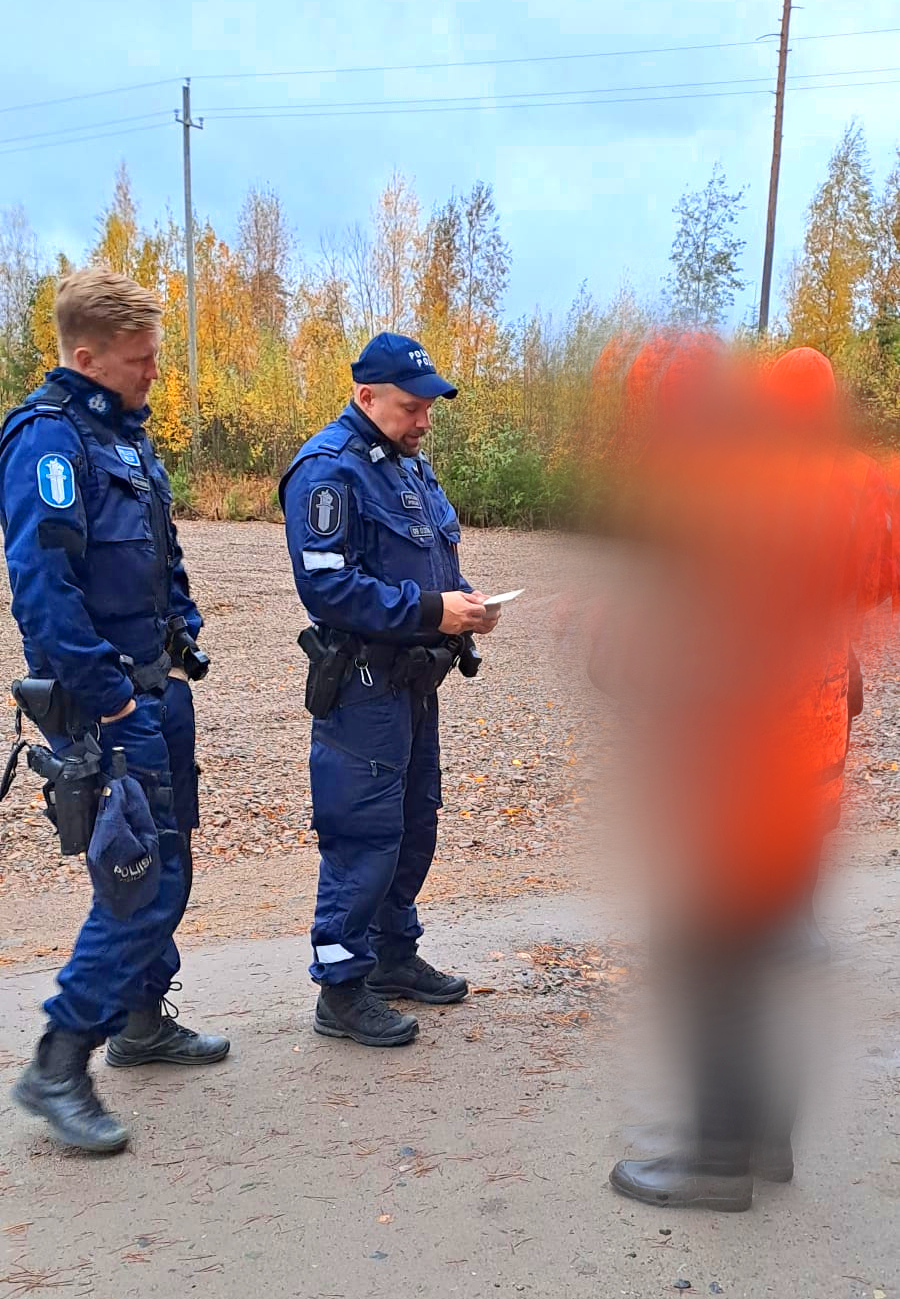 Kaksi poliisia tarkastaa oranssiin metsästysasuun pukeutuneen metsästäjän lupaa.