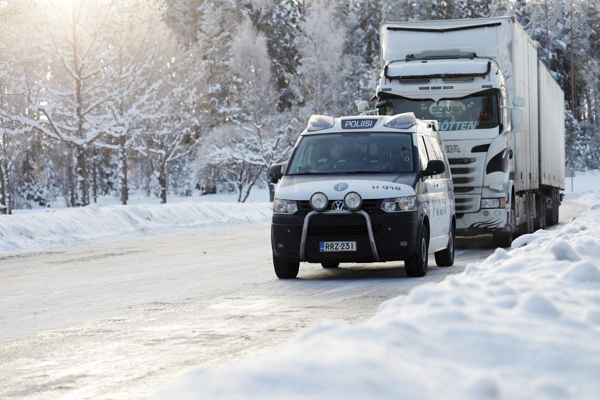 Poliisiauto yhdistelmärekan edessä moottoritien taukopaikalla talvisen aurinkoisessa säässä.