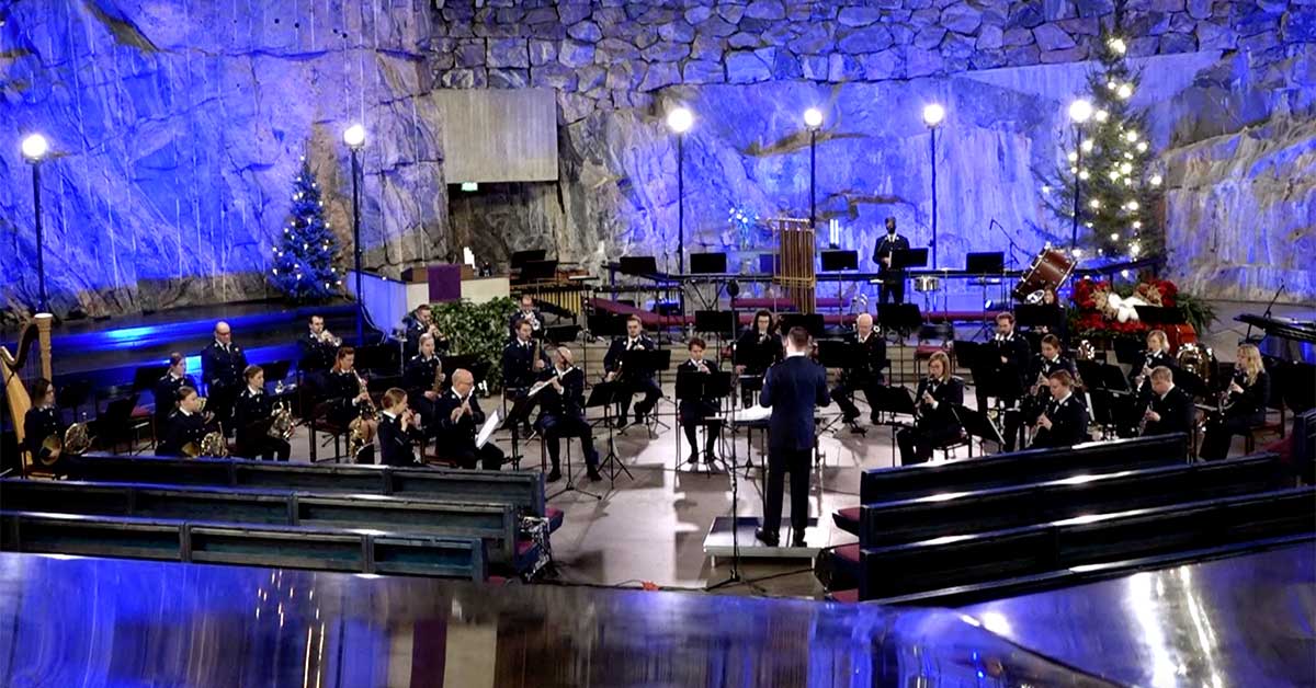 Orkesteri esiintyy kirkossa, kapellimestari seisoo keskellä johtaen soittoa. Taustalla on joulukuusi.