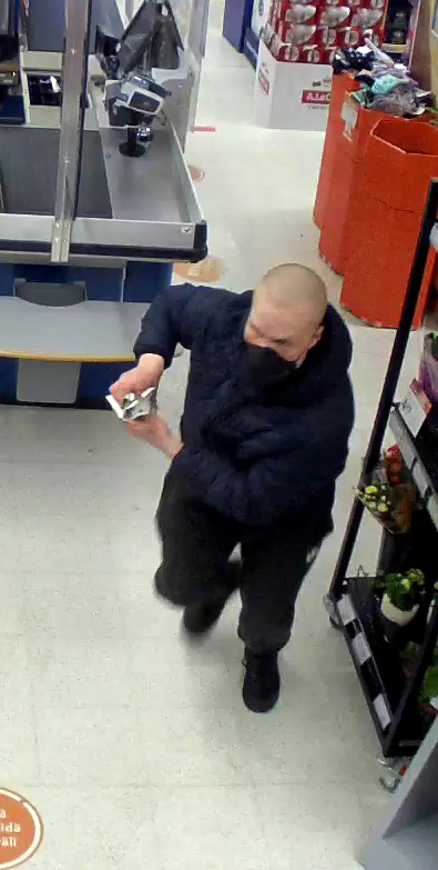 Tummiin vaatteisiin pukeutunut mies poistumassa juosten kaupasta käsissään tavaraa.