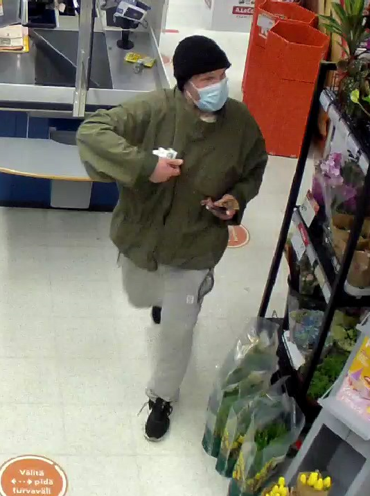 Mies vihreässä takissa ja harmaissa housuissa poistumassa kaupasta.