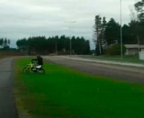 Mopoilija ajaa nurmikolla autotien ja pyörätien välillä.