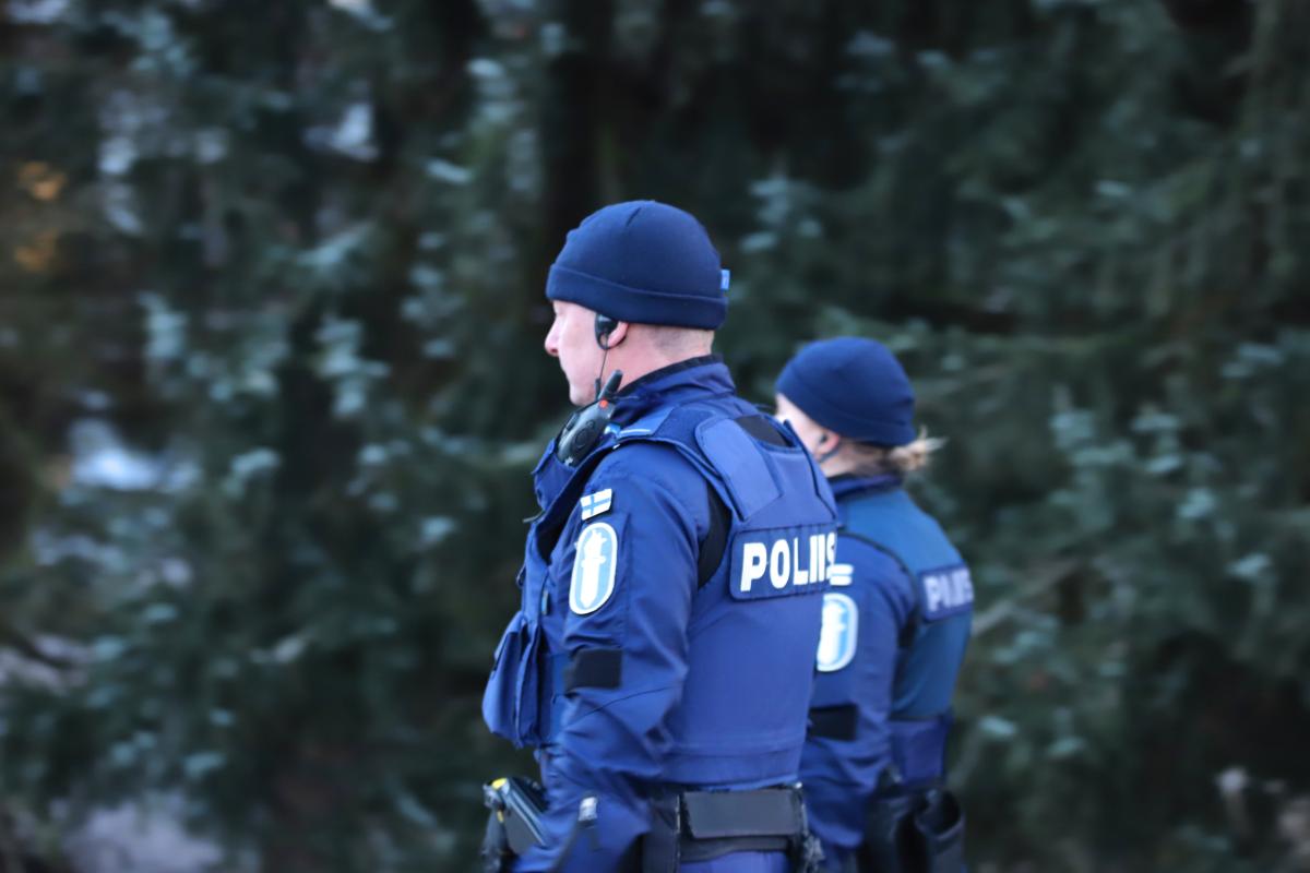 Kaksi poliisia kävelee metsäisen alueen vieressä.
