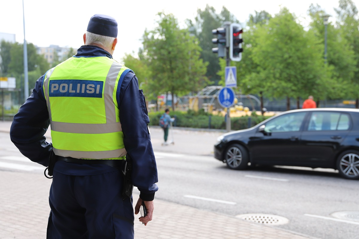Poliisimies seisoo autotien vieressä ja katsoo suojatietä ylittävää lasta.