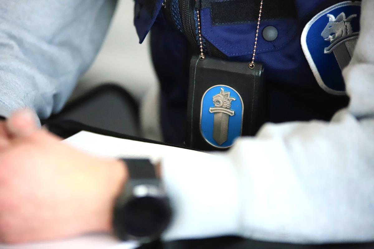 Pöydän ääressä poliisin tutkija, jolla on kaulassa tunniste.