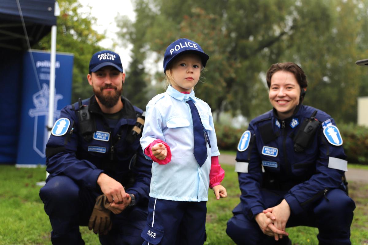 Poliisin asuun pukeutunut lapsi poseeraa kahden poliisin kanssa.