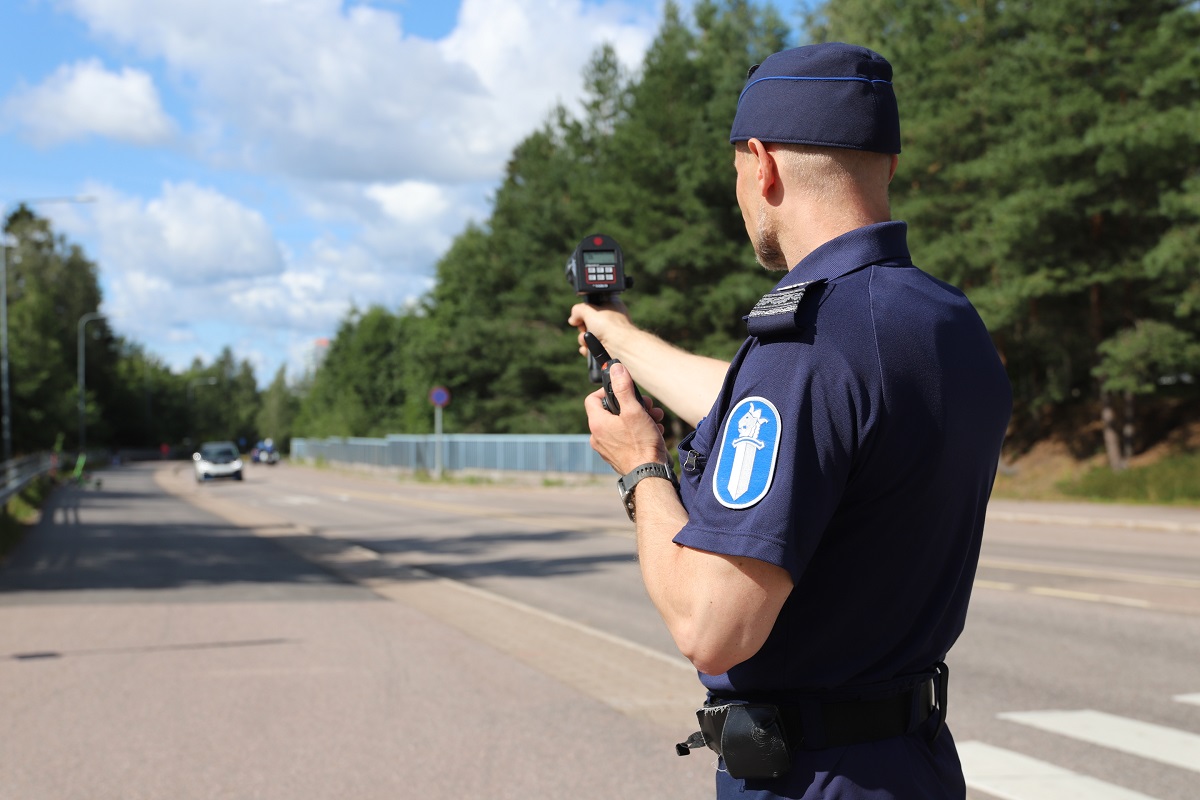 Poliisimies osoittaa tutkalla kohti autotietä, jossa lähestyy auto.