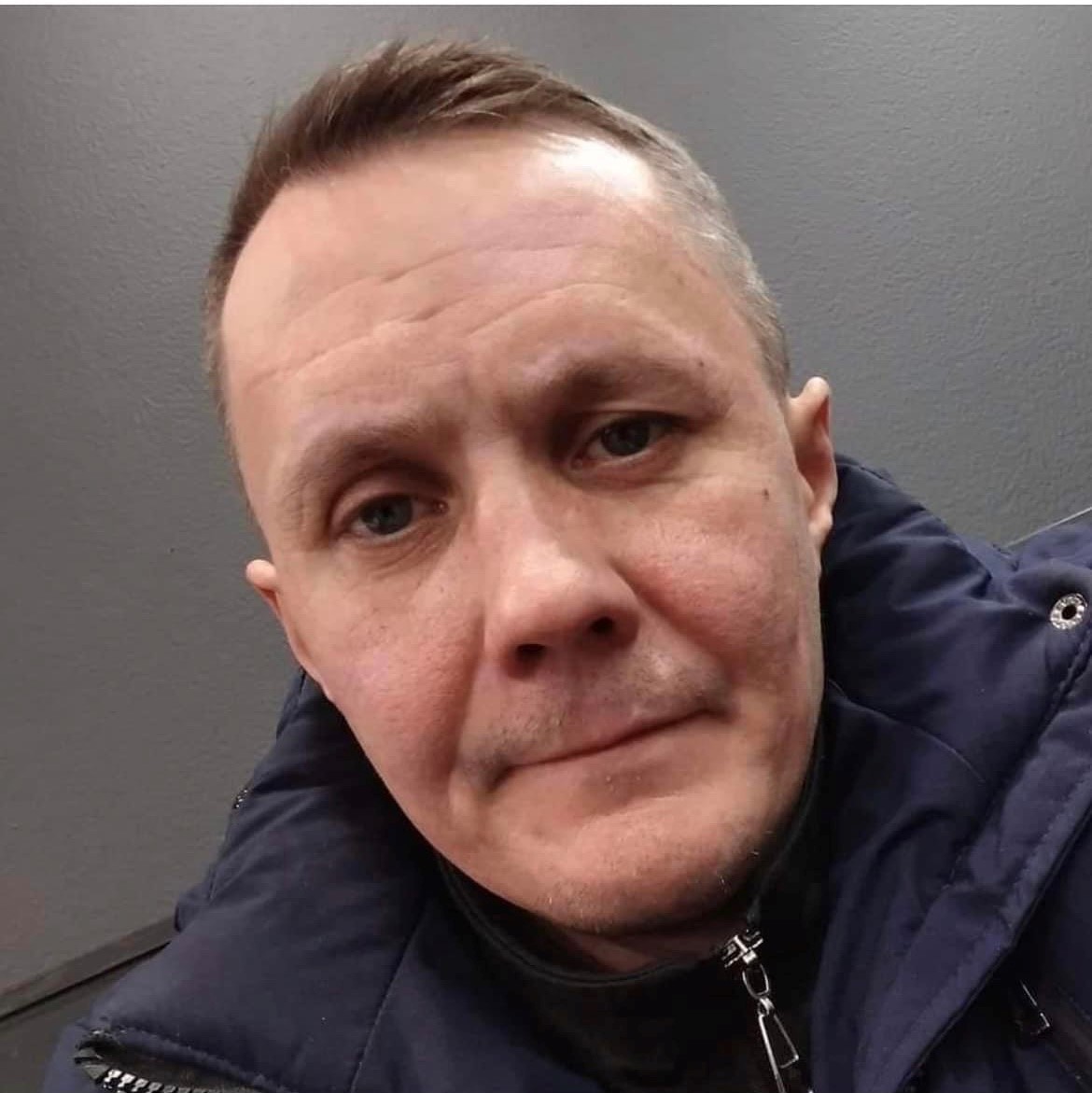 Tummahiuksinen mies mustassa takissa.