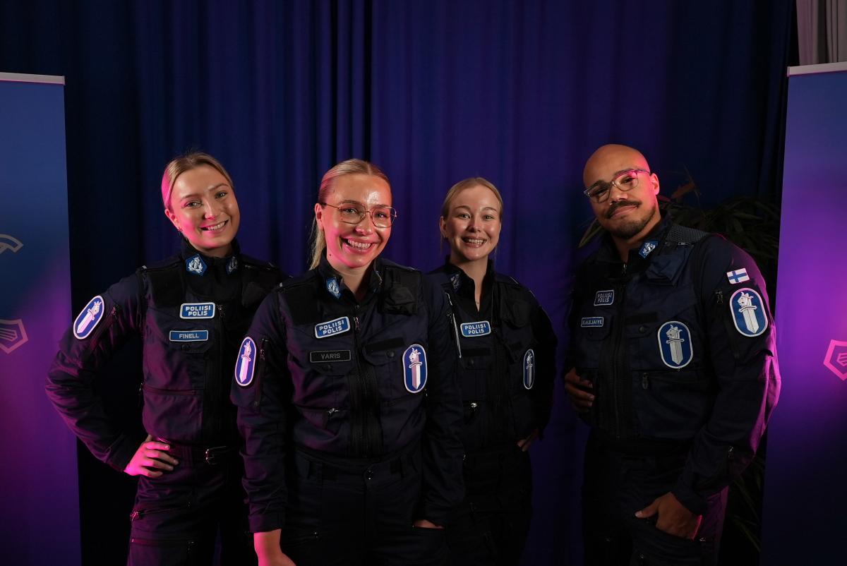 Neljä poliisia seisoo vierekkäin tummansinisen taustan edessä.