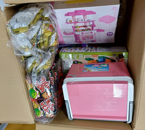 Pahvilaatikon sisällä on elintarvikkeita, vaaleanpunainen kylmälaukku ja pahvisia lelulaatikoita.