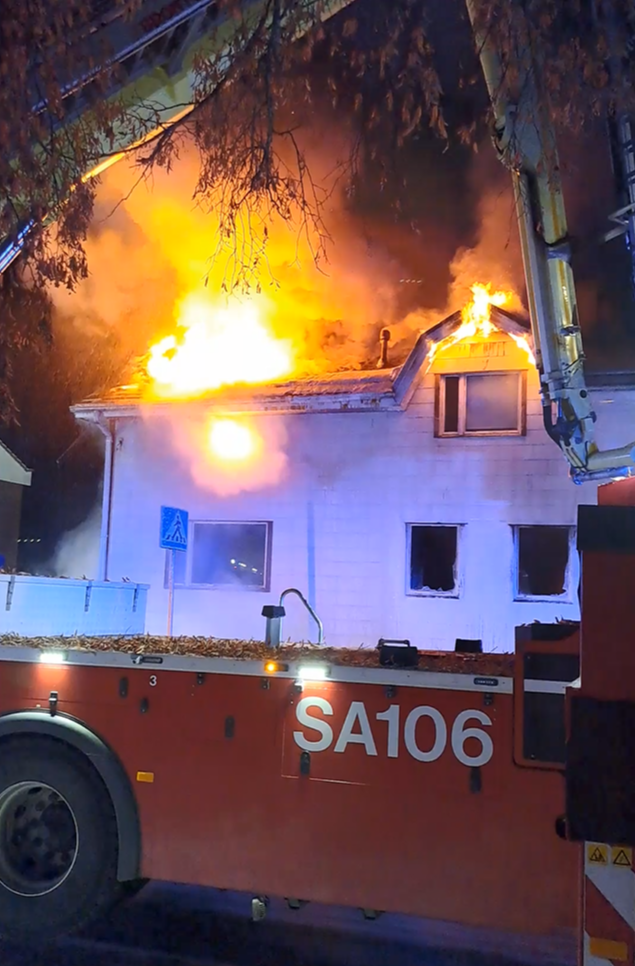 Valkoinen omakotitalo tulessa, pelastuslaitoksen nostolava-auto sammutustyössä