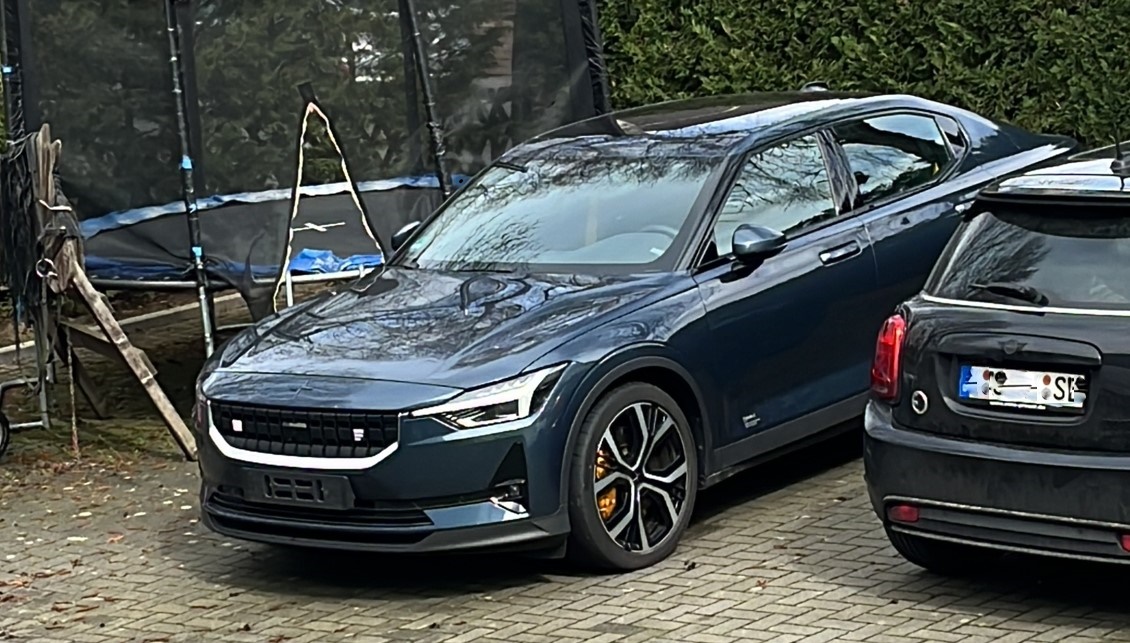 Tummanharmaa Polestar 2 -merkkinen henkilöauto, joka on pysäköity trampoliinin ja toisen auton väliin.