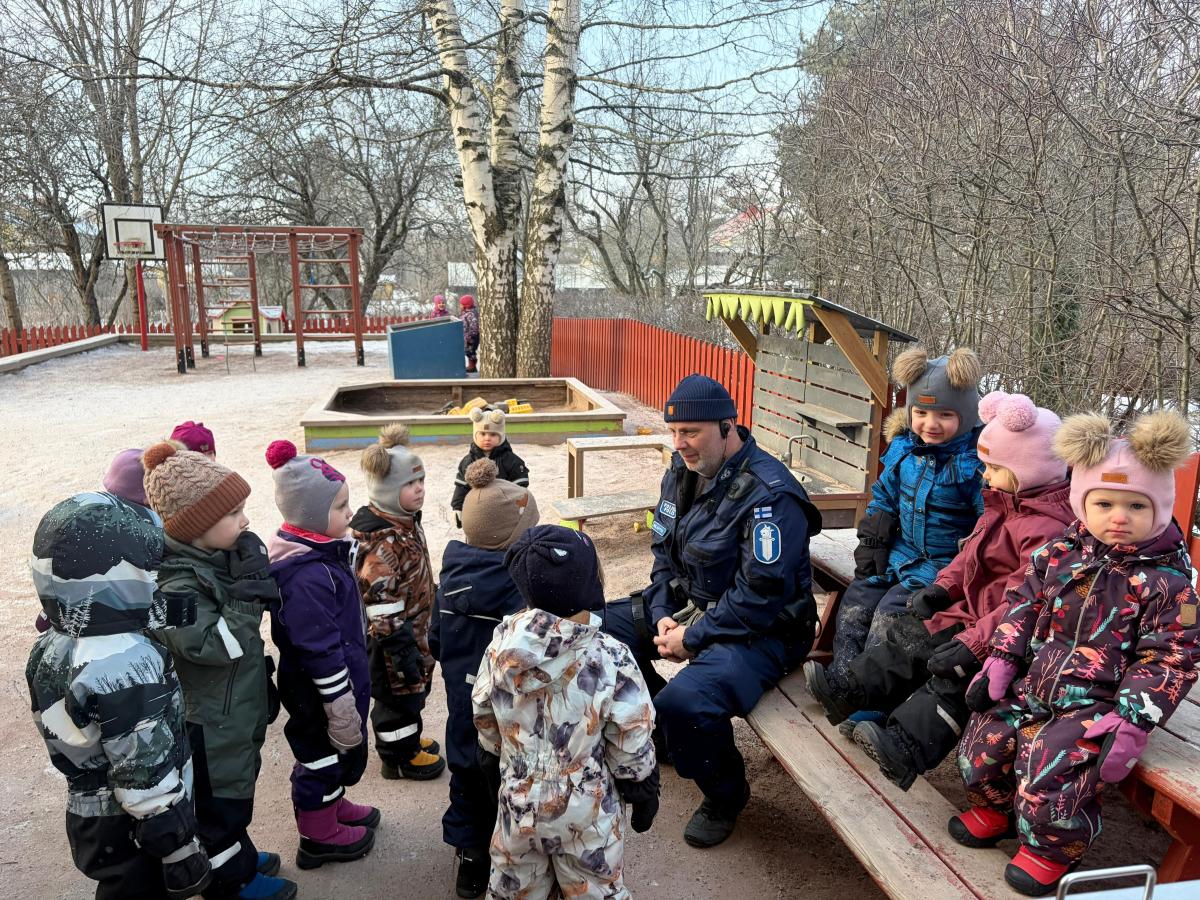 Konstapeln sitter på bänken omgiven av små barn.