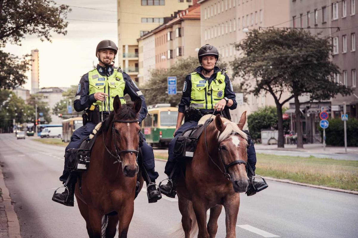 Kaksi huomioliiveihin pukeutunutta poliisia ratsastaa hevosilla kaupungissa.