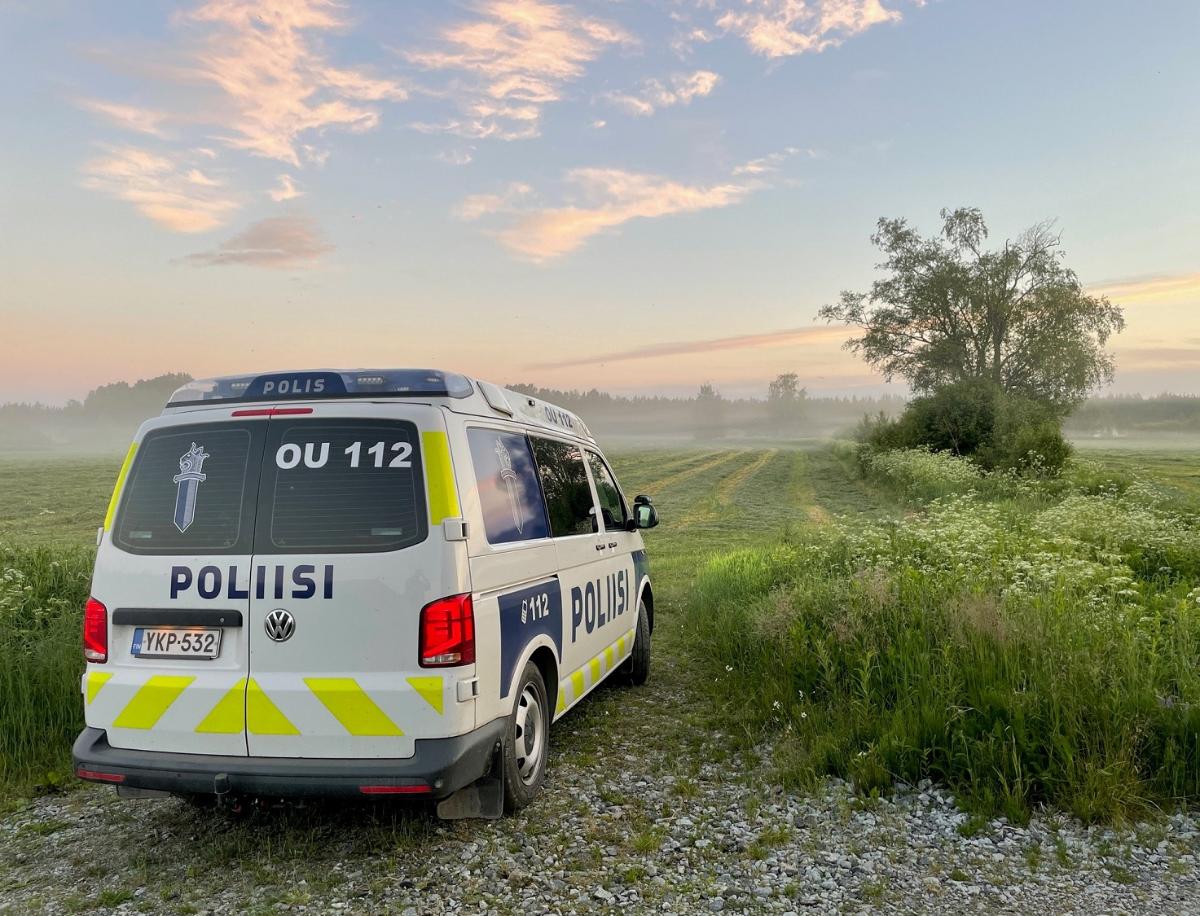Valkosininen poliisiauto pellon laidalla usvaisessa maisemassa