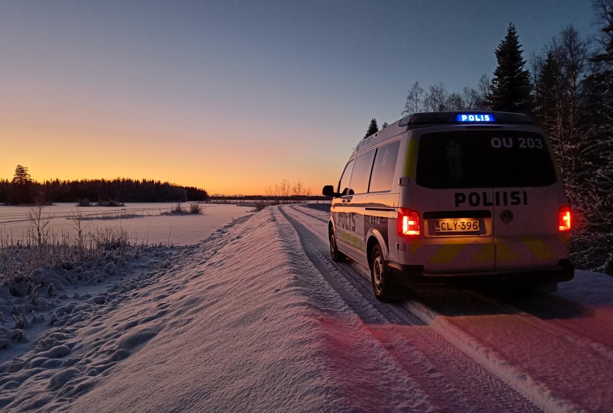 Poliisiauto lumisella tiellä pellon laidassa auringon juuri laskettua.