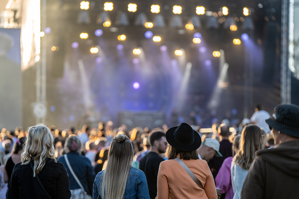 Ihmisiä selin kameraan esiintymislavan edustalla musiikkifestivaaleilla.
