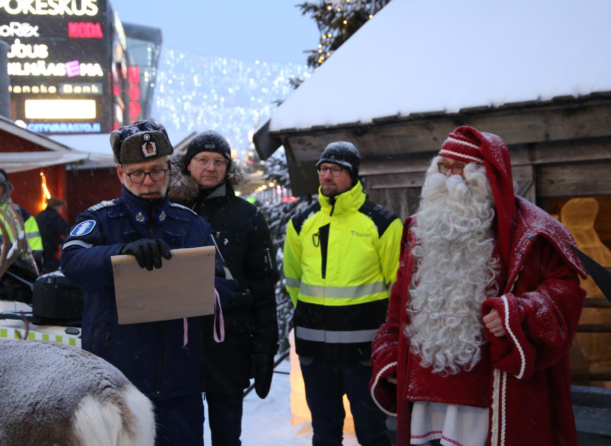 Poliisi julistaa kääröstä joulurauhan liikenteeseen yhdessä joulupukin ja kahden miehen kanssa jouluisella kävelykadulla.