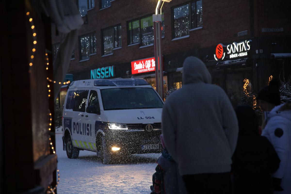 Ihmisia lumisateessa kävelykadulla ja poliisiauto ajaa vastaan