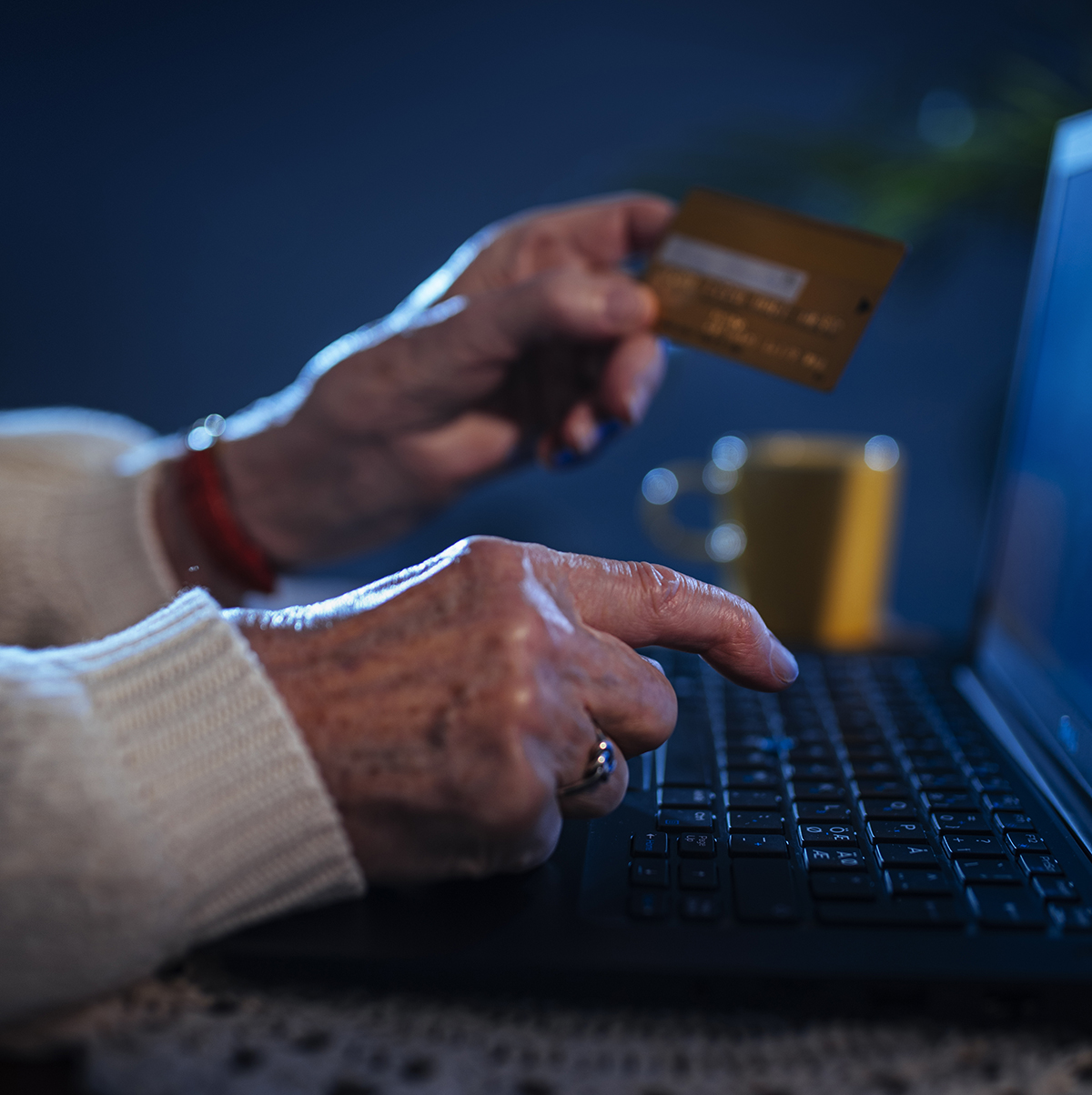 Ikääntynyt pitää kädessään pankkikorttia ja on näppäilemässä kortin numeroa läppärille.