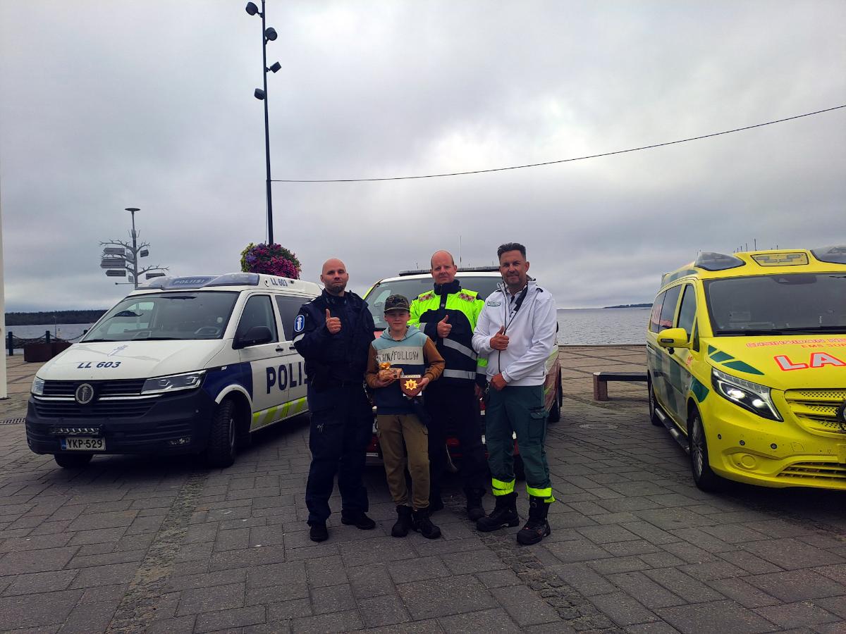 Poliisi, poika, palomestari ja ensihoidon kenttäjohtaja seisovat kolmen hälytysajoneuvon edessä.