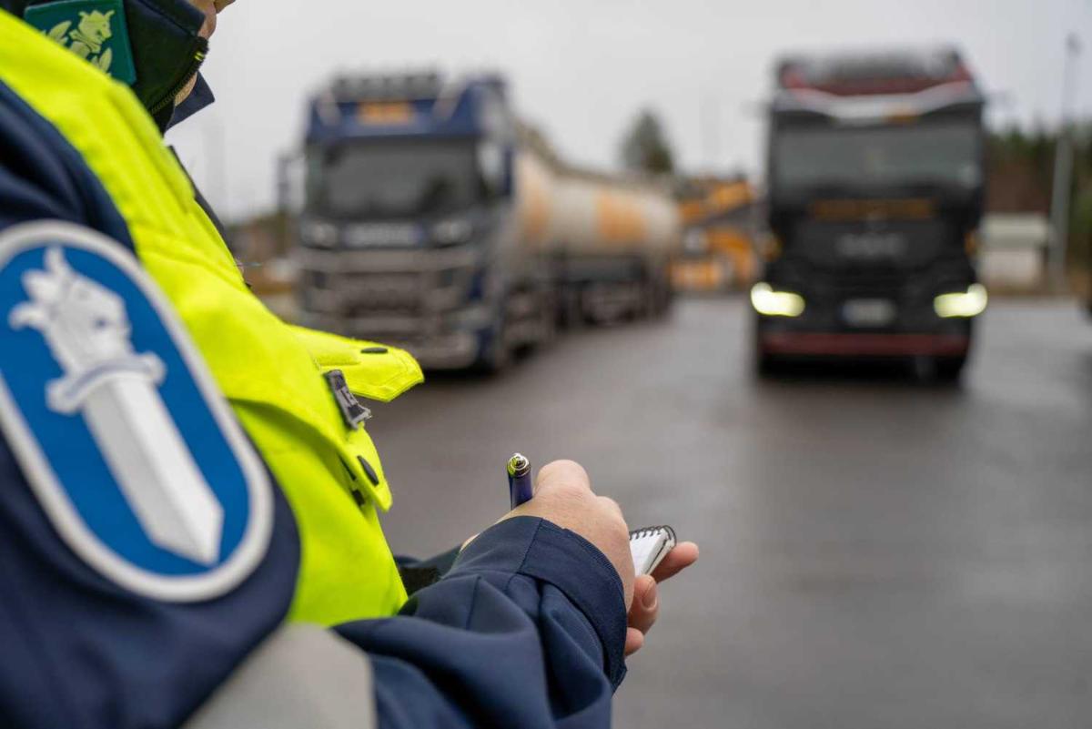 Poliisi kirjoittaa lehtiöön ja taustalla on kaksi rekka-autoa