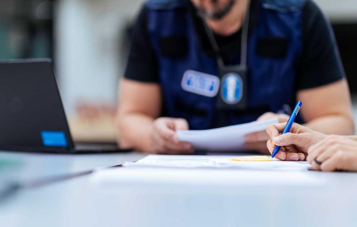Poliisi pitää kädessään paperinippua ja toinen kirjoittaa paperille