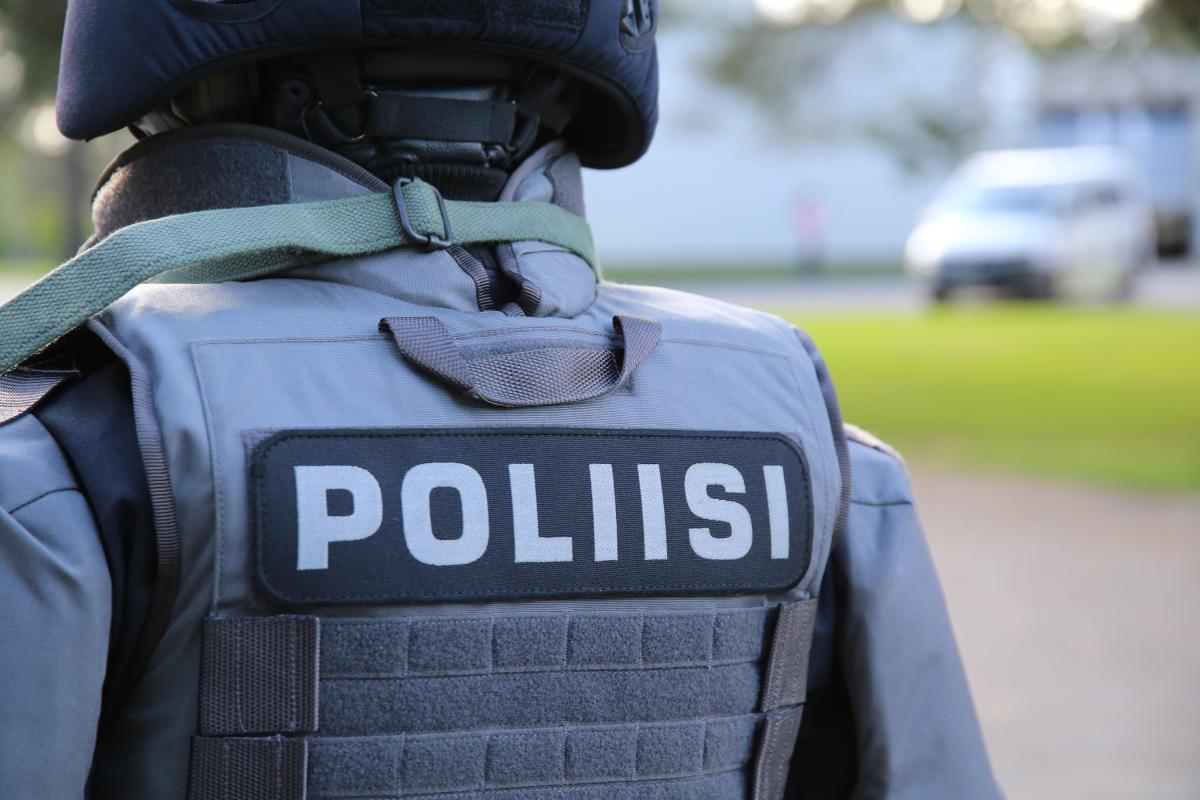 Poliisi seisoo turvavarusteissa, luotiliivissä ja -kypärässä selin.