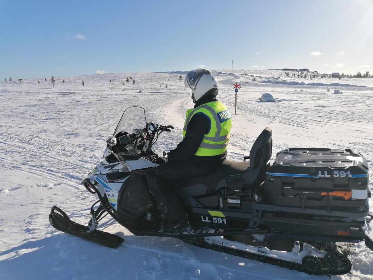 Poliisi istuu moottorikelkan päällä ja katsoo tunturiin kelkkareitin varrella