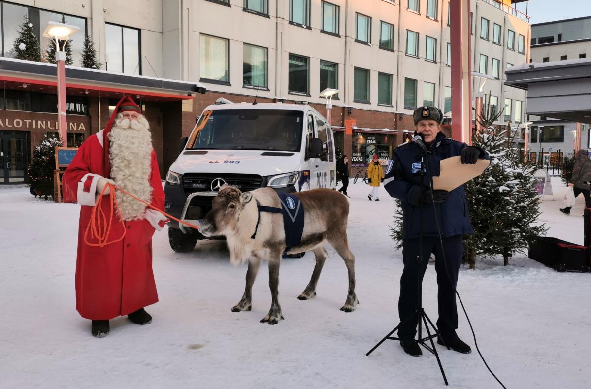 Poliisipäällikkö pitää kädessään julistusta ja puhuu. Vierellä ovat joulupukki ja poro, takana iso poliisiauto.