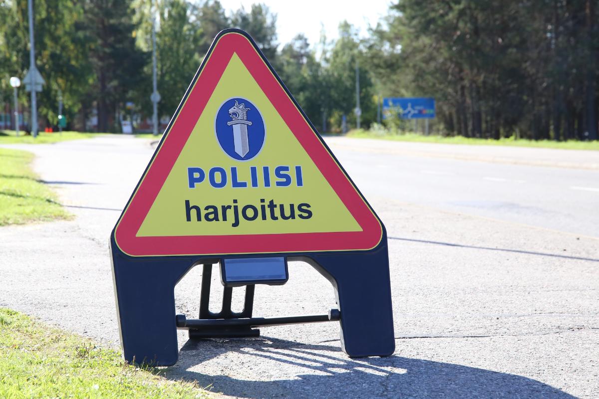 Varoituskolmiossa, joka seisoo tien laidassa, on alekkain tekstit poliisi ja harjoitus.