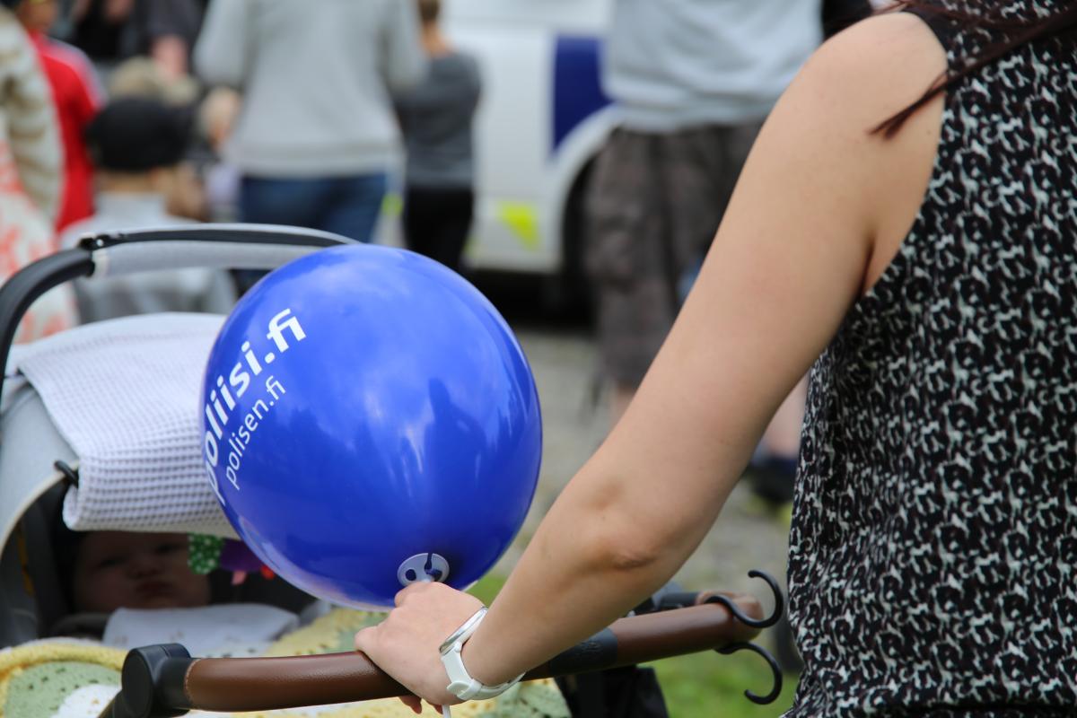 Nainen työntää lastenvaunuja kädessään poliisin ilmapallo.