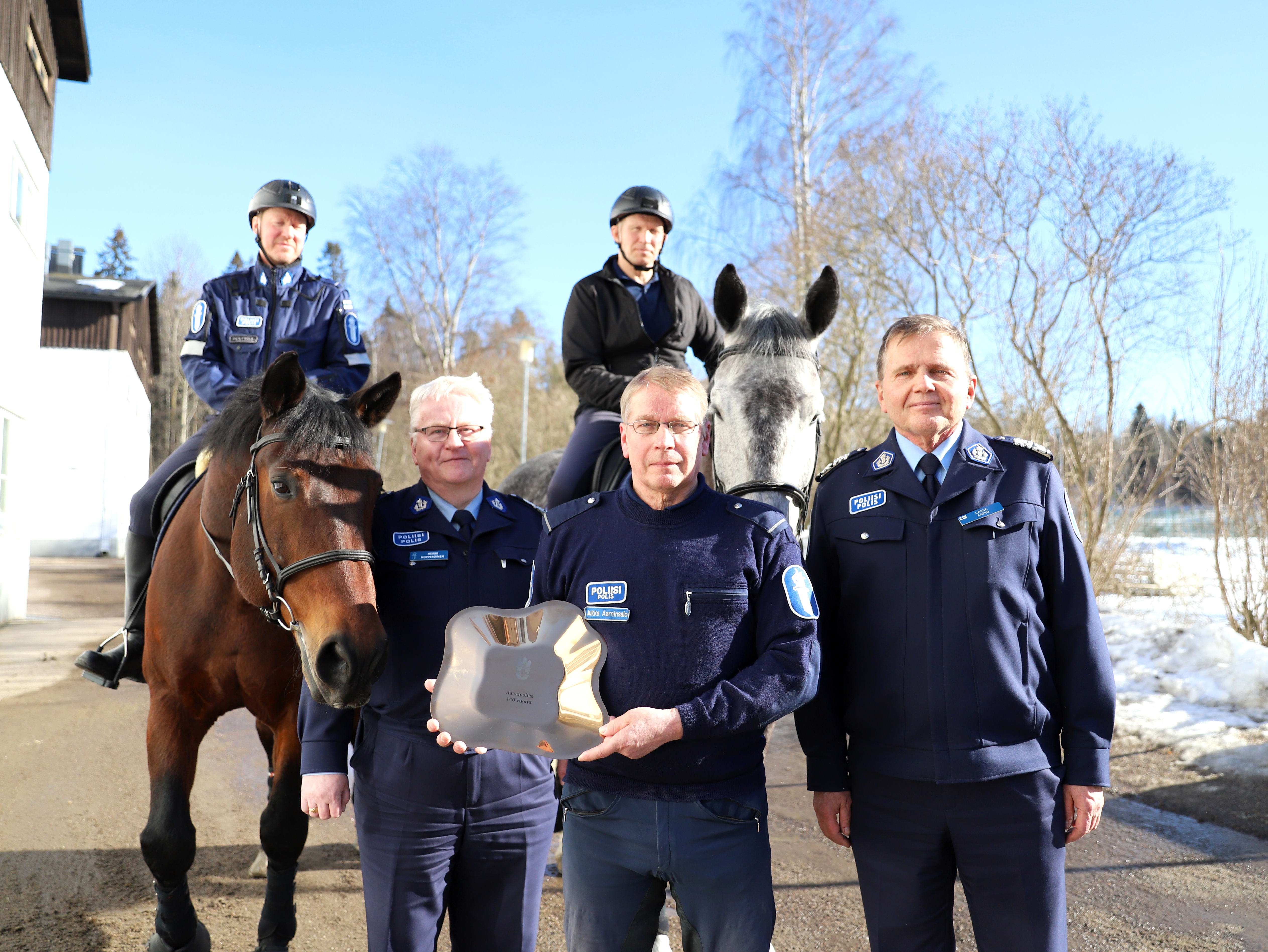 Taustalla kaksi poliisihevosta ja hevospoliisia. Edessä kolme poliisia.