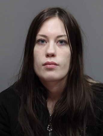 Nainen katsoo kameraan. Tummat pitkät hiukset, vaalea iho ja musta huppari.