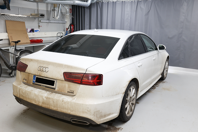 Valkoinen henkilöauto hallissa takaa.